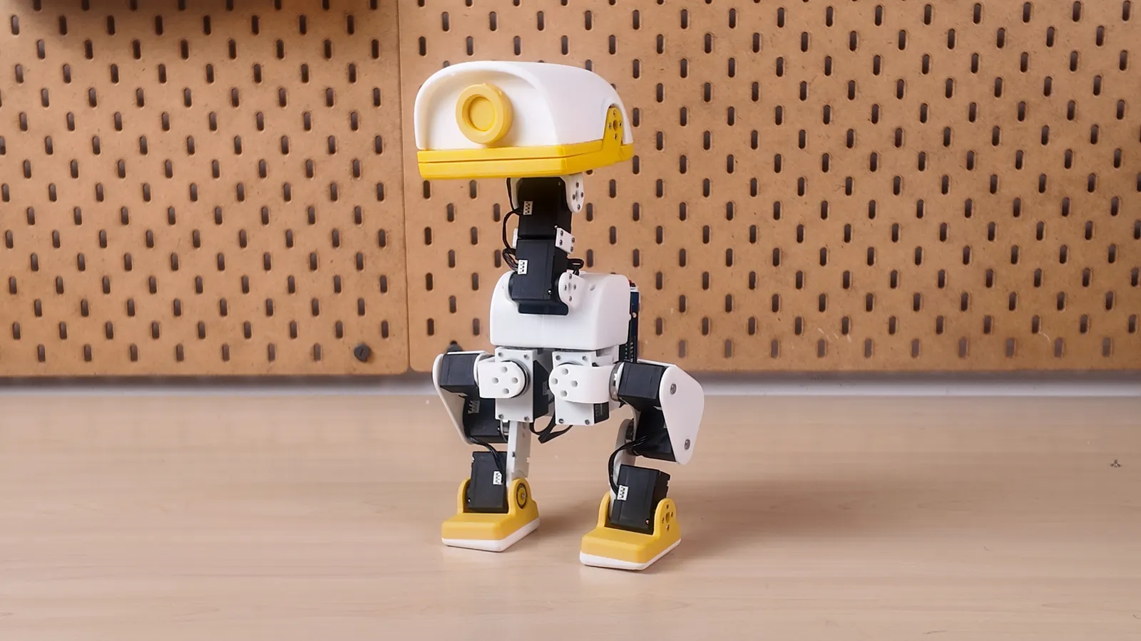 作業台の上に立つ XGO-Duck。白い3Dプリントの胴体と脚、黄色のくちばしと足